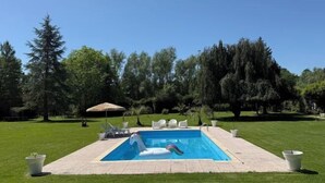 A rectangular swimming pool with a white inflatable unicorn float, surrounded by a paved deck and potted plants.