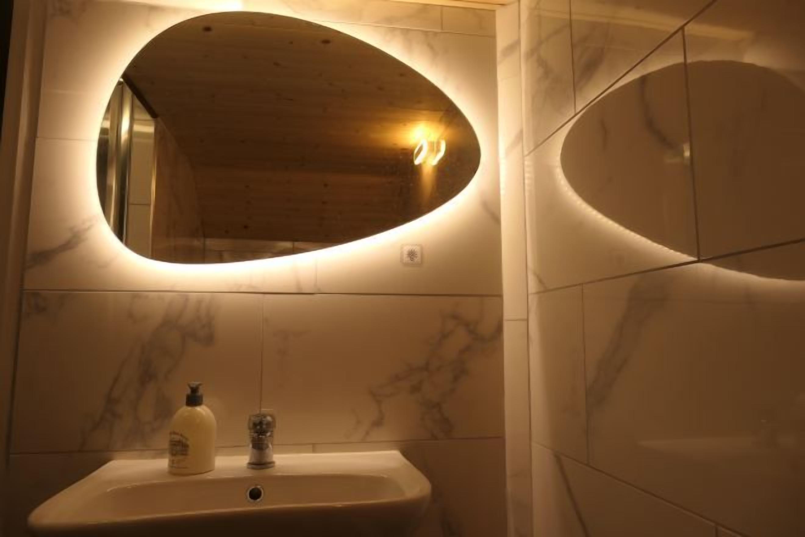 Un bagno con un lavandino in marmo, uno specchio con cornice ovale e una bottiglia di sapone per le mani.