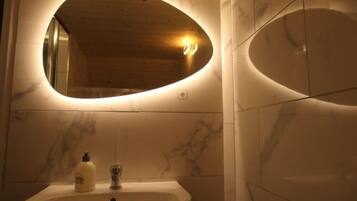 Un bagno con un lavandino in marmo, uno specchio con cornice ovale e una bottiglia di sapone per le mani.