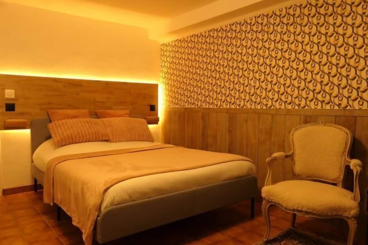 Une chambre à coucher avec une tête de lit en bois, un lit recouvert d’une couvre-lit beige et une chaise assortie.