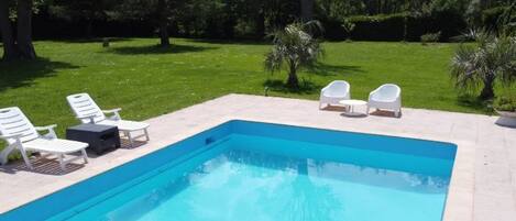 Una piscina rectangular con solárium empedrado, rodeada de sillones blancos y una pequeña mesa.