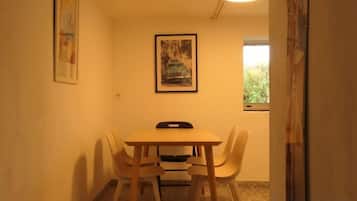 Uma pequena sala de jantar com uma mesa e quatro cadeiras, uma luminária no teto e duas imagens emolduradas nas paredes.