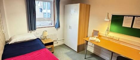 Ein Zimmer mit einem Bett, einem Schreibtisch, einem Stuhl, einem Kleiderschrank, einem Fenster mit Vorhängen und einer grünen Wandtafel.