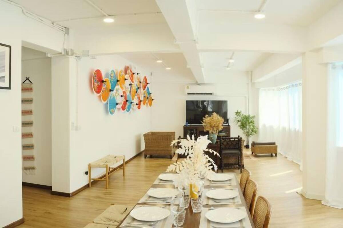 Un comedor con una mesa larga dispuesta para seis comensales, un televisor y una pared con obras de arte coloridas.