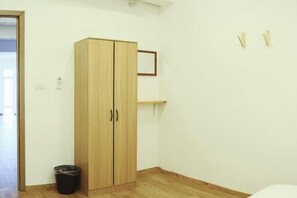 Une pièce avec une armoire en bois, une petite poubelle et une étagère fixée au mur.