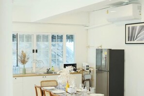 Una cocina moderna con una mesa de comedor para dos personas, un refrigerador y una ventana con vistas a árboles.