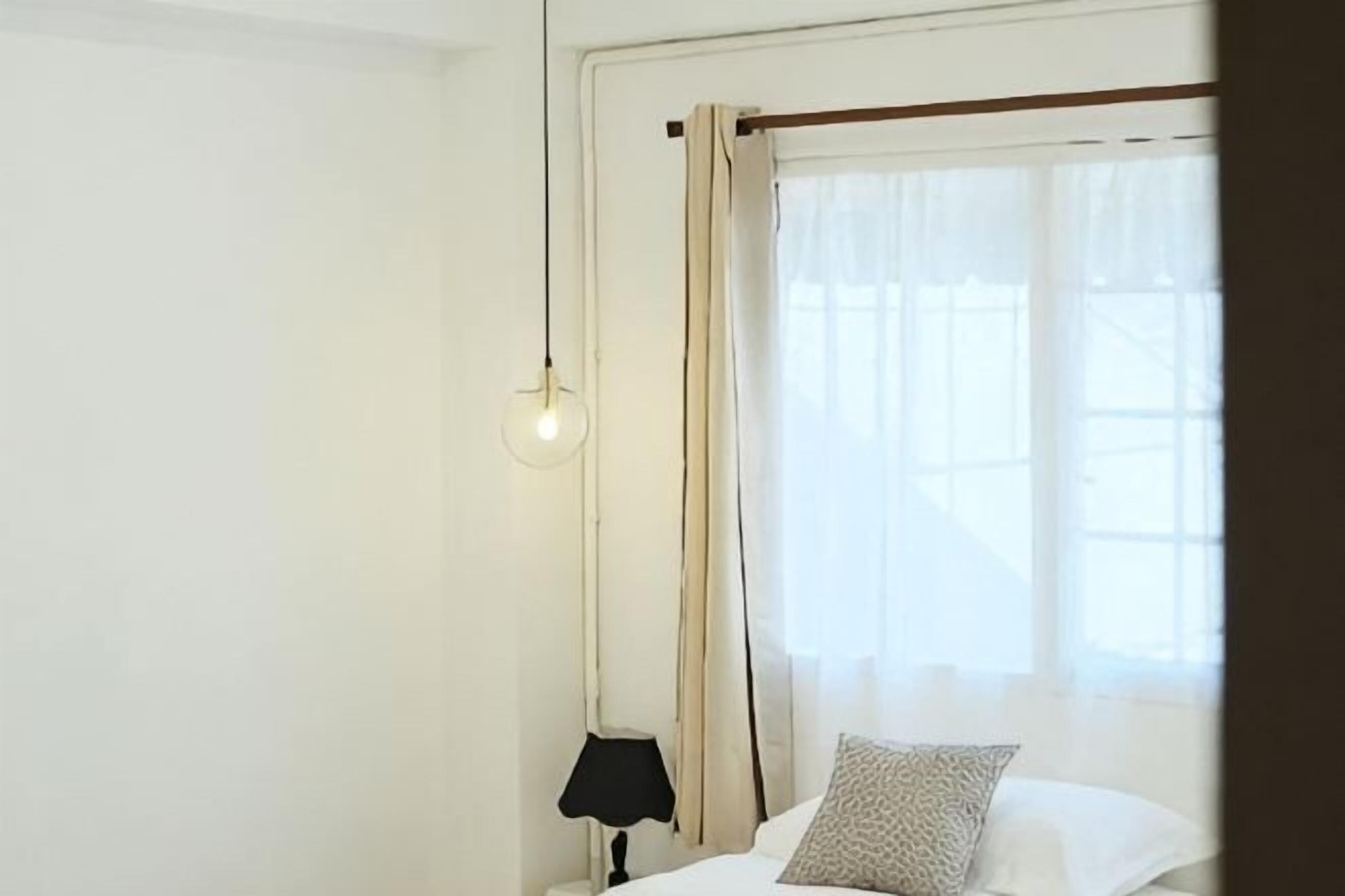 A room with a bed, a nightstand, a lamp, and a window with curtains.
