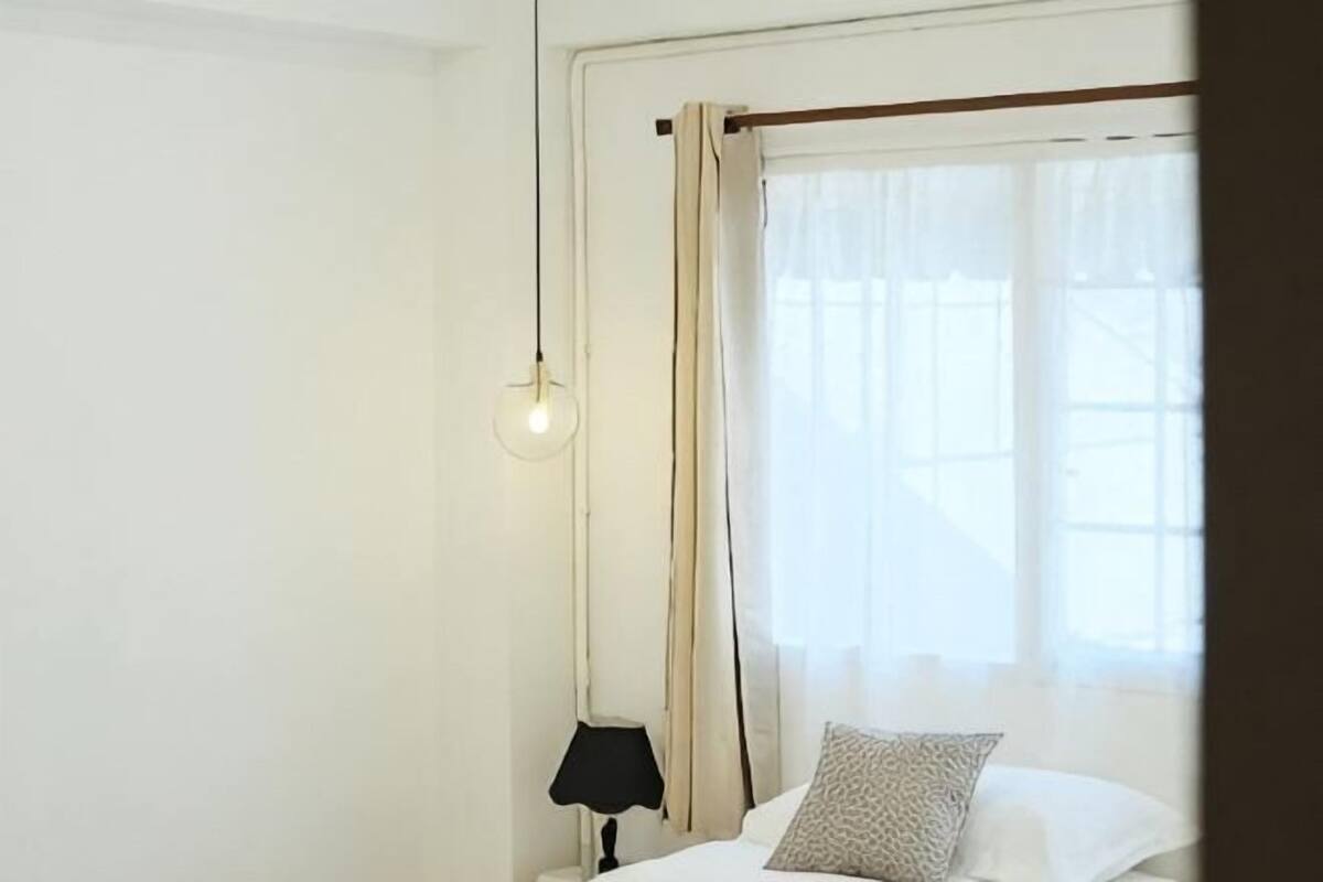 Una habitación con cama, mesita de noche, lámpara y ventana con cortinas.