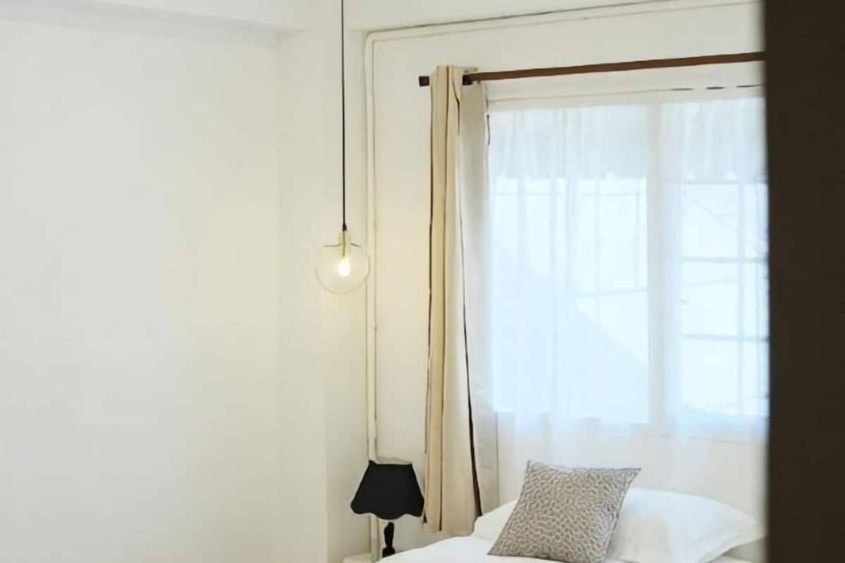 A room with a bed, a nightstand, a lamp, and a window with curtains.