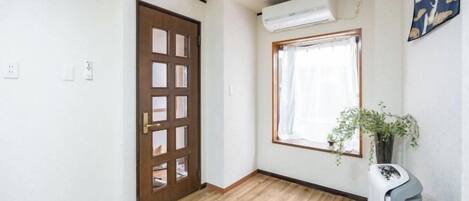 A room with a wooden floor, a door, a window with a plant, and a wall-mounted air conditioner.