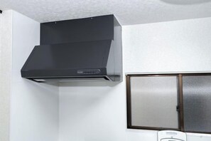 A kitchen with a black range hood and a window with a metal screen. - Kaike・Honcho detached house (Tokyo)