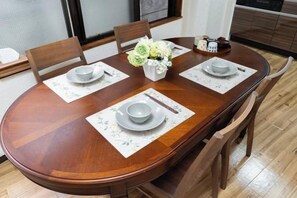 A wooden dining table set with plates, bowls, chopsticks, and a vase of flowers. - Kaike・Honcho detached house (Tokyo)