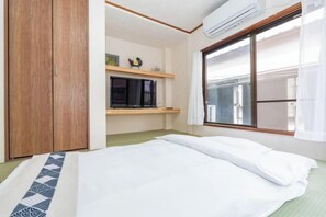 A bedroom with a bed, a wooden wardrobe, a shelf with a TV, and a window with blinds. - Kaike・Honcho detached house (Tokyo)