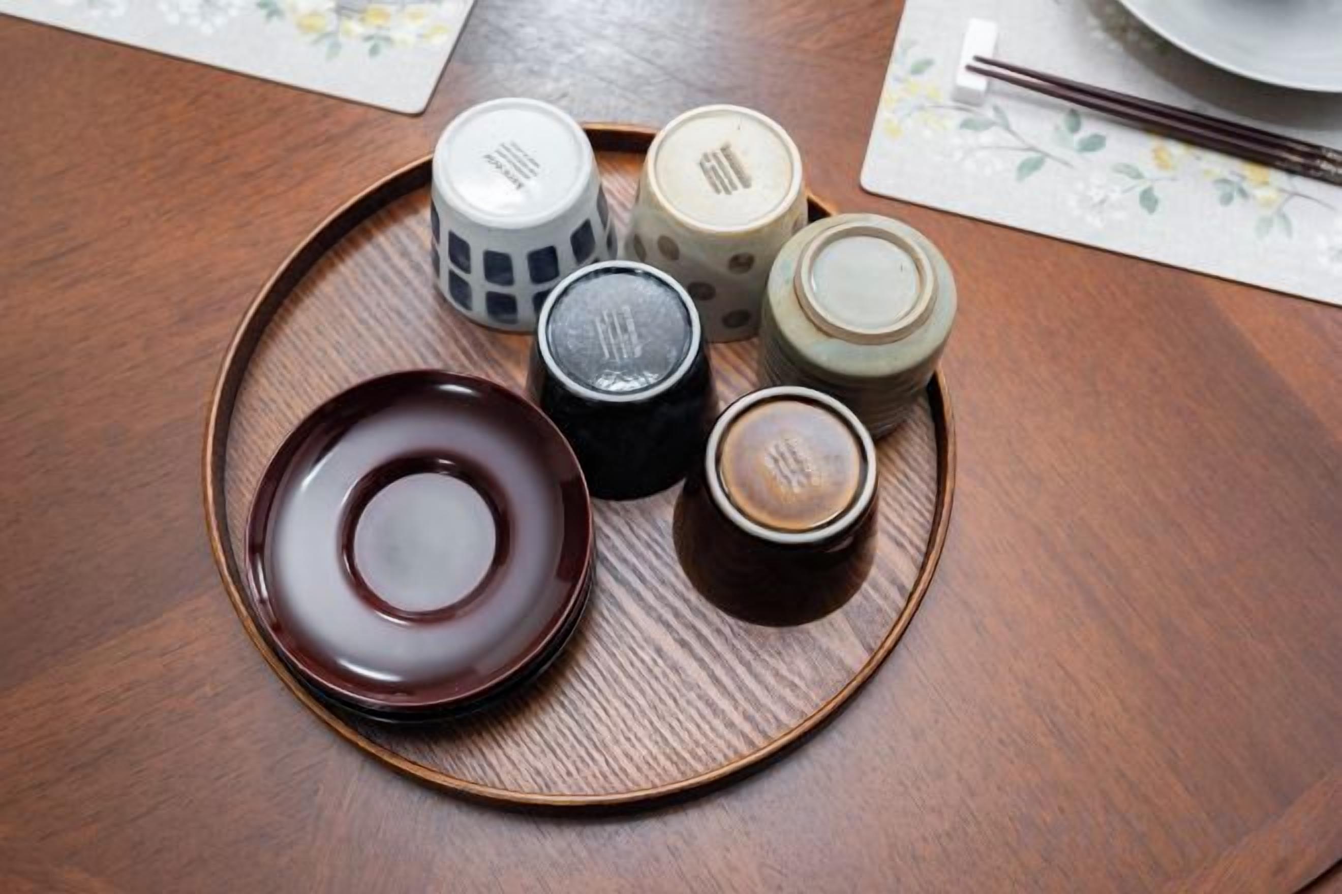 Une table en bois avec une assiette, quatre tasses et des baguettes.