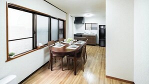 A compact kitchen with modern appliances, a dining area with a wooden table and chairs, and a large window providing natural light. - Kaike・Honcho detached house (Tokyo)