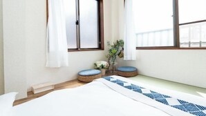A bedroom with a bed, two windows, a small plant, and a white curtain. - Kaike・Honcho detached house (Tokyo)