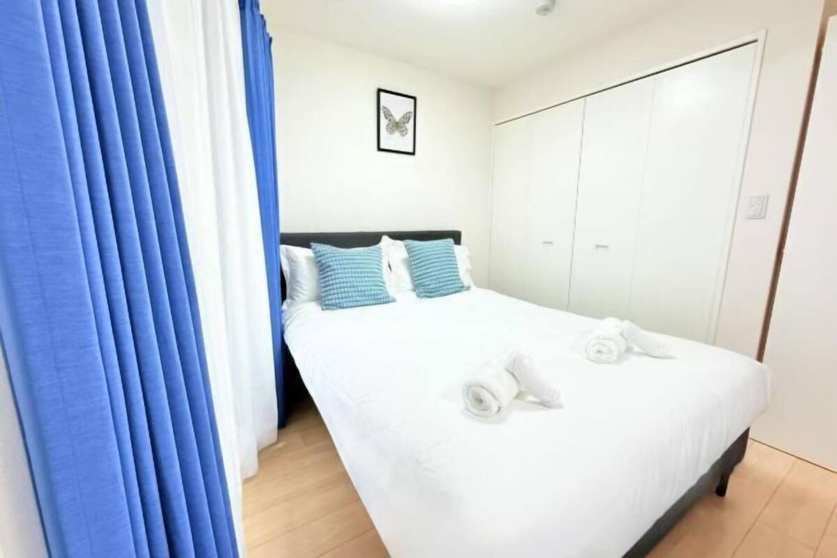 A neatly made bed with white bedding and blue accents, a framed butterfly artwork on the wall, and a set of white lockers to the right.