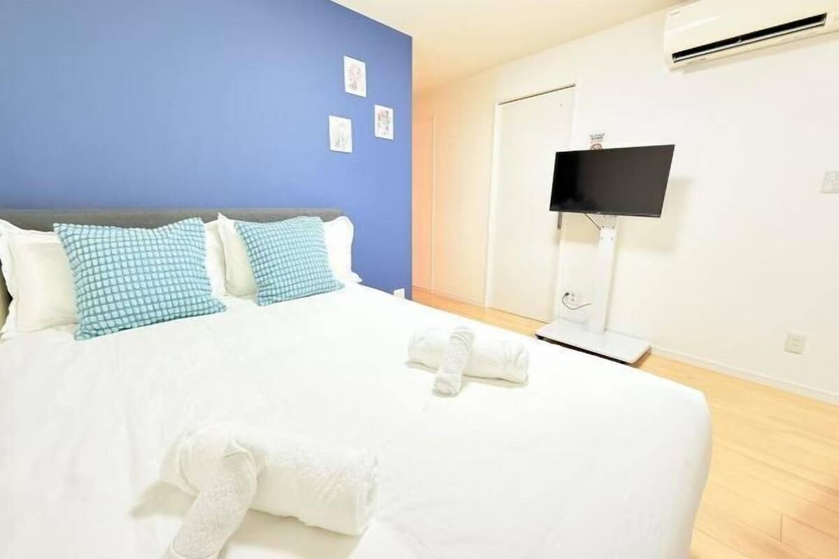 A hotel room with a bed, blue and white checkered pillows, a white blanket, and a TV mounted on the wall.
