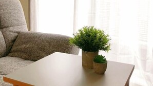 Een woonkamer met een grijze bank, een witte salontafel en twee potplanten.