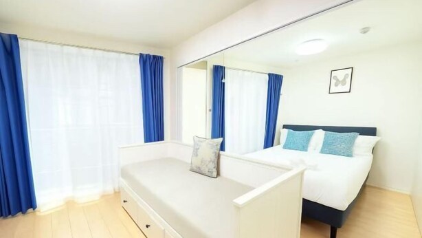A bedroom with a bed, a bedside table, a mirror, and a window with curtains. - BASE36 (Tokyo)