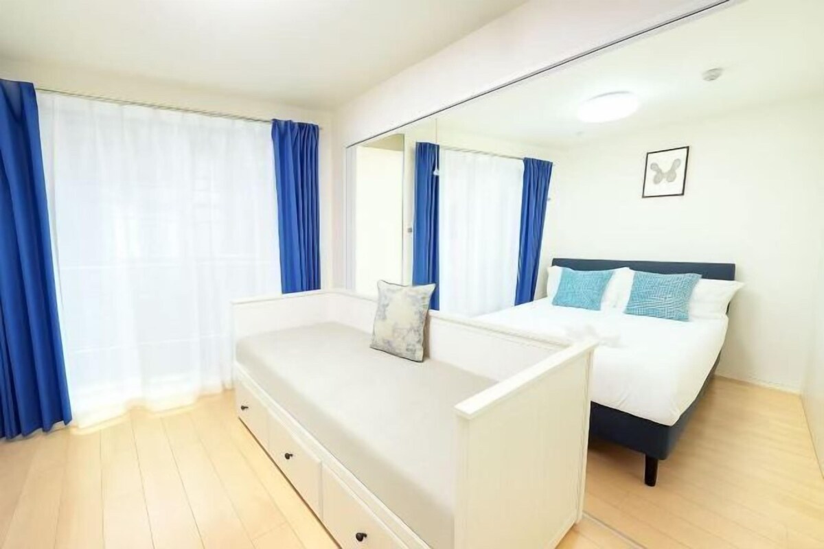 A bedroom with a bed, a bedside table, a mirror, and a window with curtains.