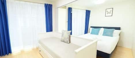 Un dormitorio con cama, mesita de noche, espejo y ventana con cortinas.