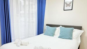 A neatly made bed with white linens, two pillows with a checkered pattern, and a framed butterfly artwork on the wall. - BASE36 (Tokyo)