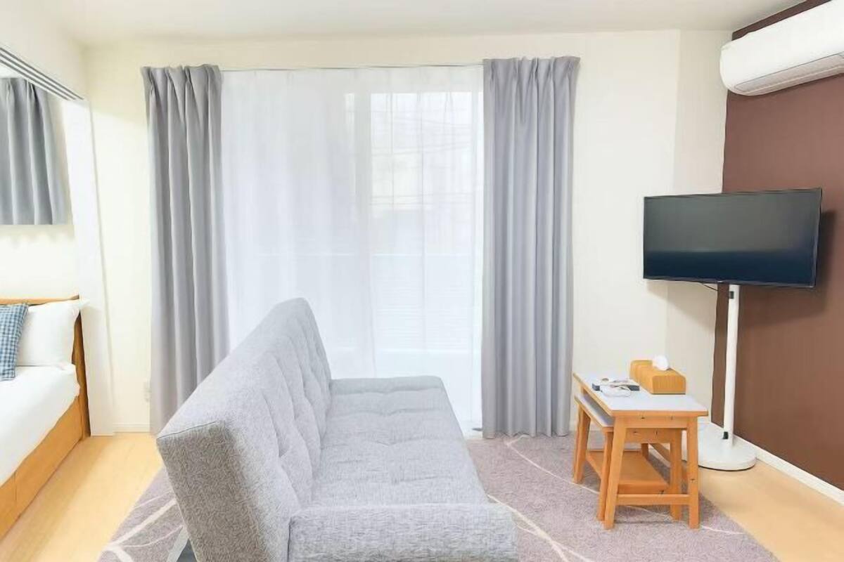 A hotel room with a sofa, a TV, a small table, and curtains.