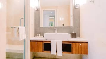 A modern bathroom with a glass shower enclosure, a white sink, wooden cabinets, and a large mirror.