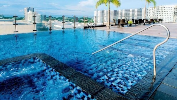 A swimming pool with a clear view of the ocean and palm trees, surrounded by hotel buildings. - MCollection - Convenient City Stay in Iloilo Business Park (Iloilo City)