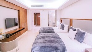 A modern hotel room with a flat-screen TV, a wooden accent wall, a large bed with grey bedding, and a small desk with a chair. - MCollection - Convenient City Stay in Iloilo Business Park (Iloilo City)
