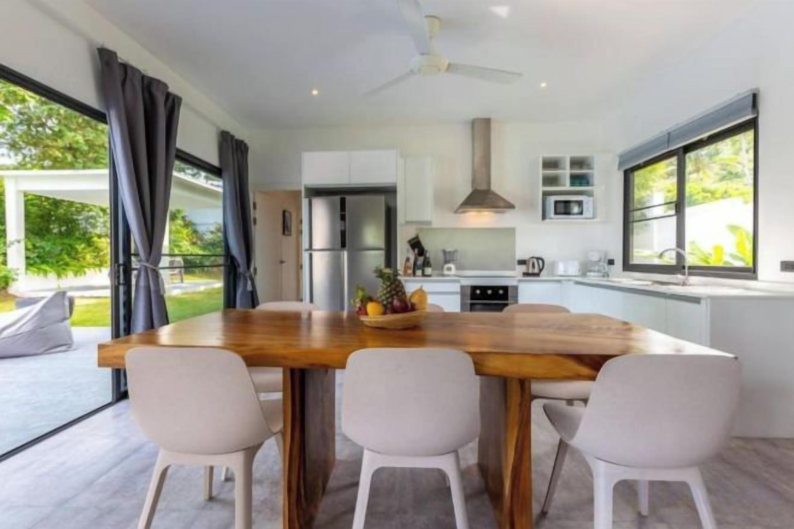 A modern kitchen with a central island, white cabinetry, and a dining area with chairs.