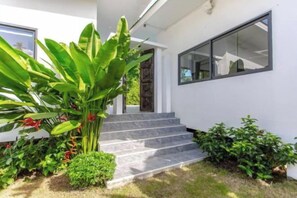 A modern house with a white exterior, a set of stairs leading to a door, and a large window on the right side. - Villa Lotus, 3 Bedrooms (Koh Samui)