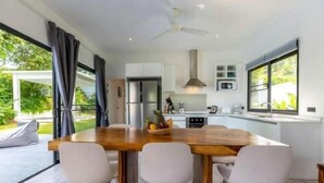 A modern kitchen with a wooden dining table, white chairs, and a large window. - Villa Lotus, 3 Bedrooms (Koh Samui)