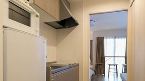 Een compacte keuken met een magnetron, oven en een inbouwafzuigkap. In de aangrenzende ruimte staan een krukje en een stoel.
