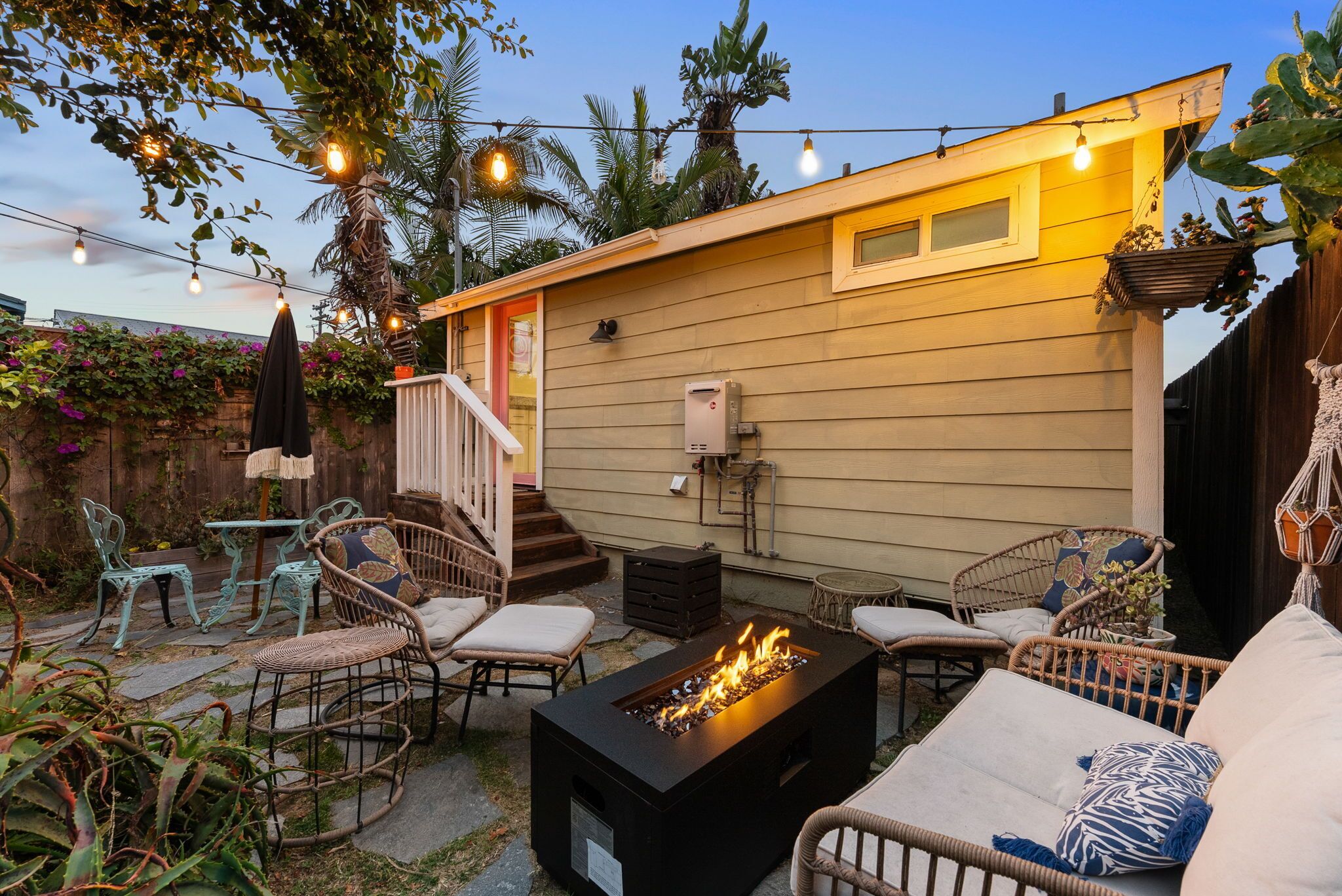 A backyard with a fire pit, outdoor furniture, and string lights.