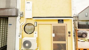 A yellow building with a ventilation system, a circular window, and a door with a vent. - KIN'S HOUSE (Osaka)