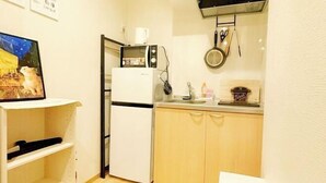 A compact kitchen with a refrigerator, microwave, sink, and wooden cabinets. - KIN'S HOUSE (Osaka)