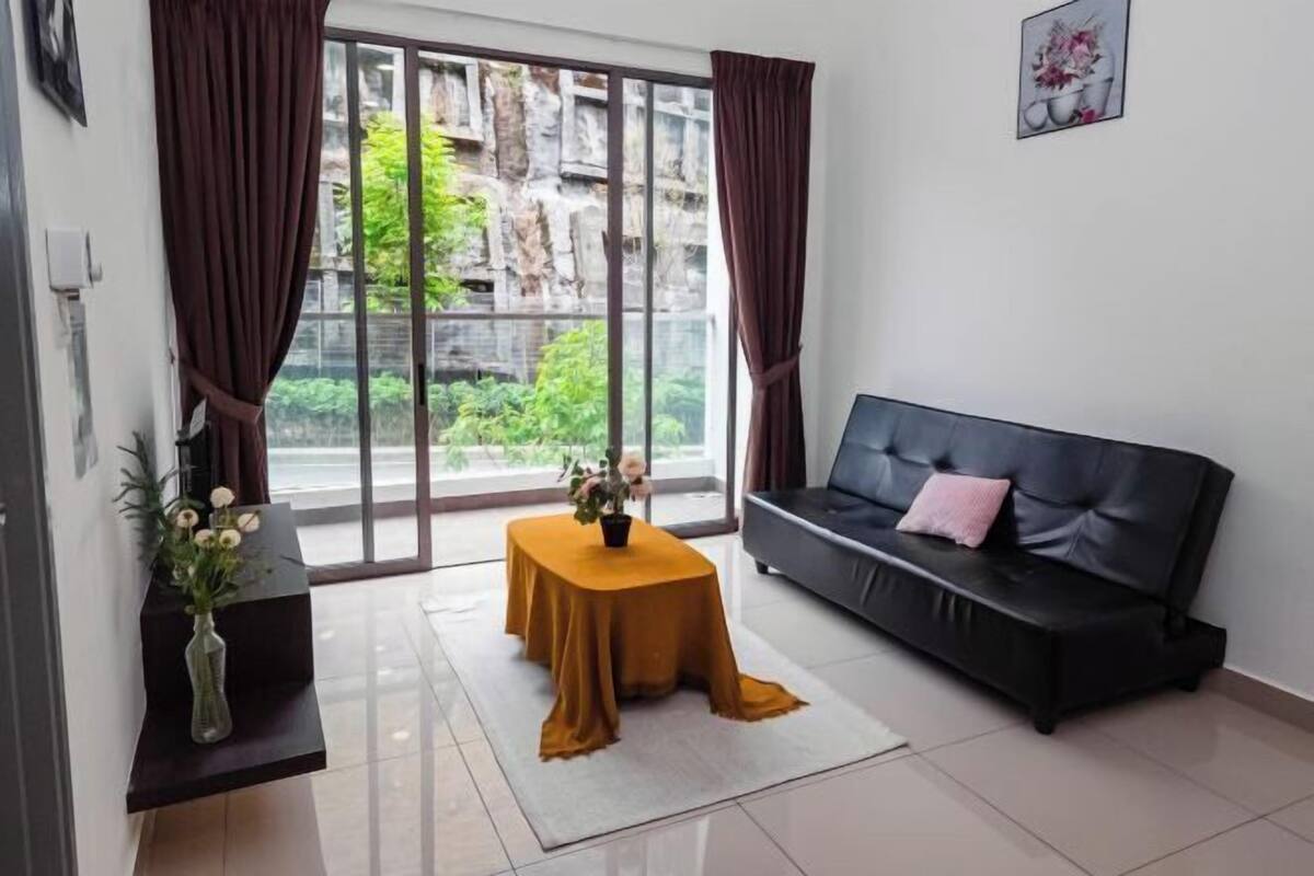 Een moderne woonkamer met een zwarte bank, een klein tafeltje met een gele tafelkleed en een vaas met bloemen.
