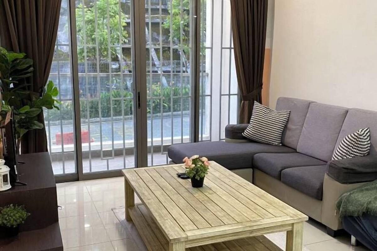 Een woonkamer met een grijze bank, een houten salontafel met een plant, en uitzicht door grote glazen deuren.