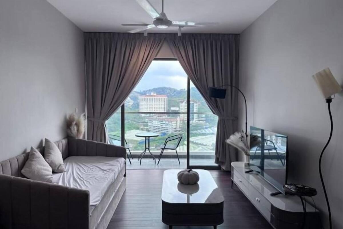 Een moderne hotelkamer met een bank, een salontafel, een televisie en een balkon met uitzicht op gebouwen en groen.