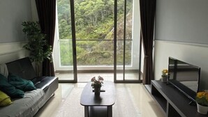 Una sala de estar con un sofá, una mesa de centro, un televisor y un ventanal con vistas a la vegetación.
