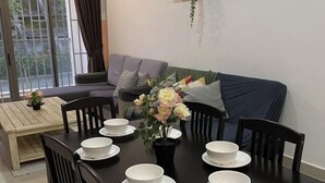 Un comedor con una mesa dispuesta para cuatro personas, rodeada de sillas, un sofá y una planta con flores.