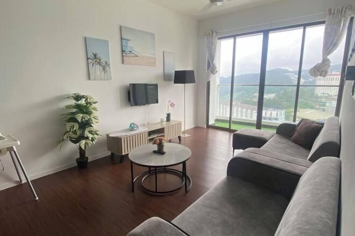 Een moderne woonkamer met een groot raam, een grijze bank, een klein rond tafeltje en een plant in pot.