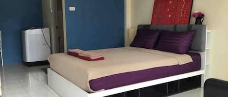 A bed with a white frame, a red and beige bedspread, and purple pillows.
