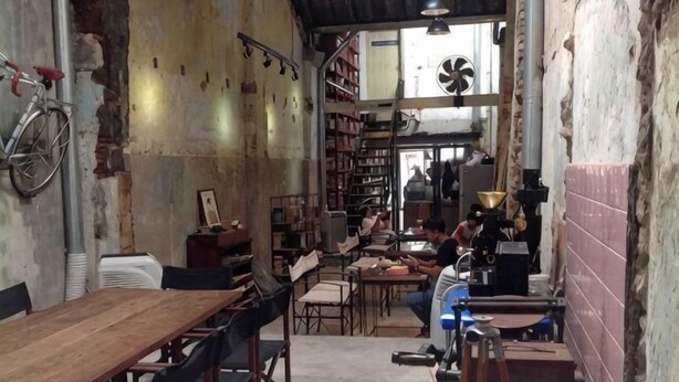 A rustic interior with wooden tables and chairs, a bicycle, and a fan. - Phuket Town Budget House - Aircon Room #1 (Phuket)