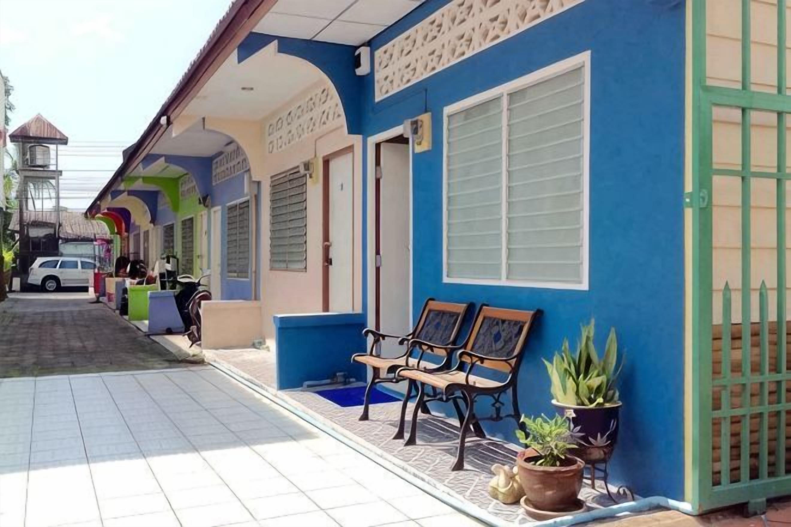 A building with a blue exterior, a covered porch with benches, and potted plants.