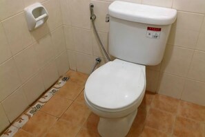 A standard white toilet with a flush handle and a bidet attachment in a small bathroom with tiled walls and floor. - Phuket Town Budget House - Aircon Room #1 (Phuket)