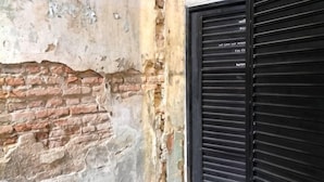 A brick wall with peeling paint and a black metal shutter door. - Phuket Town Budget House - Aircon Room #1 (Phuket)