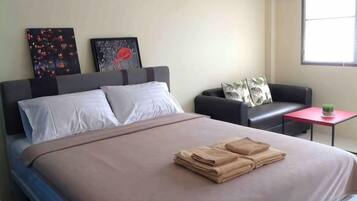 Cama bem arrumada com toalhas dobradas, um sofá, uma mesinha com uma planta e obras de arte na parede.